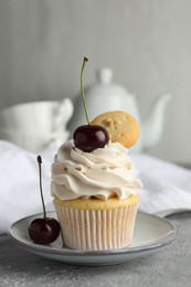 Photo of Delicious cupcake with cherries and cookie on grey textured table, closeup