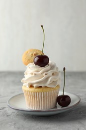 Photo of Delicious cupcake with cherries and cookie on grey textured table, closeup