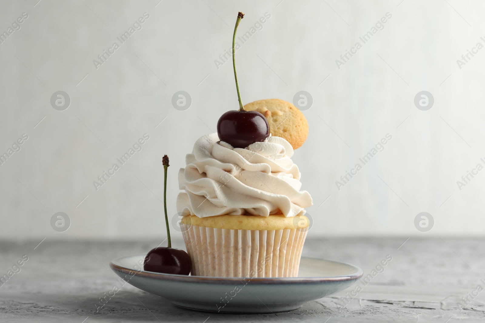 Photo of Delicious cupcake with cherries and cookie on grey textured table, closeup