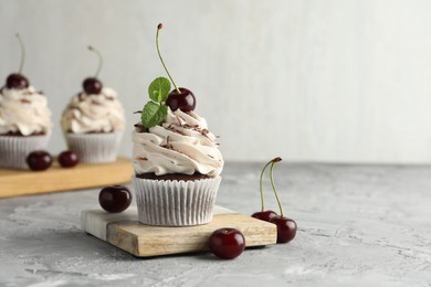 Photo of Delicious cupcake with cream and cherries on grey textured table, space for text