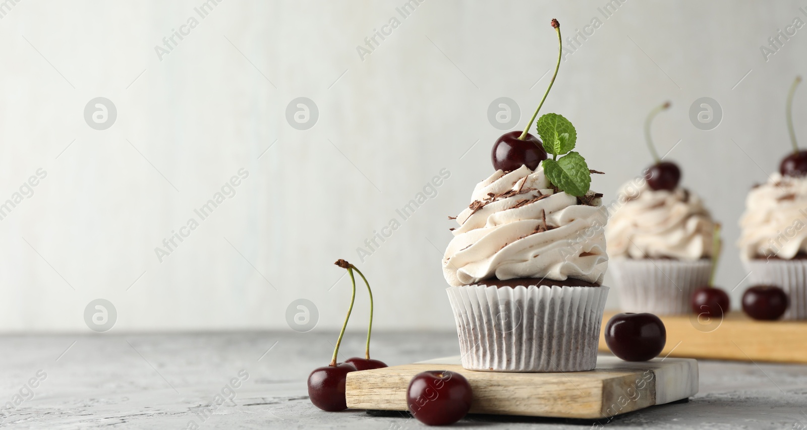 Photo of Delicious cupcake with cream and cherries on grey textured table, space for text