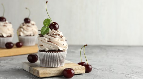 Delicious cupcake with cream and cherries on grey textured table, space for text