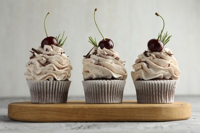 Photo of Delicious cupcakes with cream and cherries on grey textured table, closeup