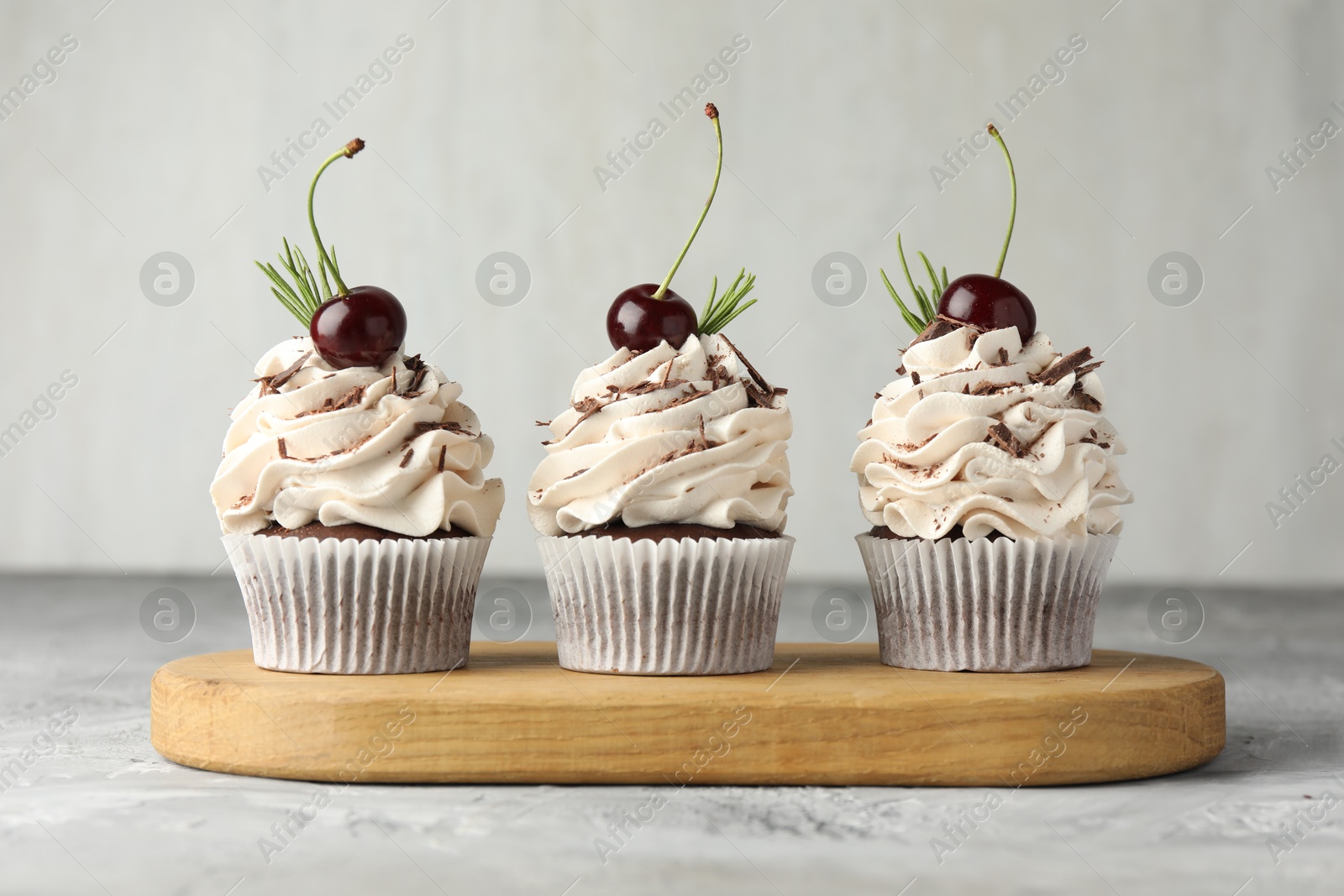 Photo of Delicious cupcakes with cream and cherries on grey textured table