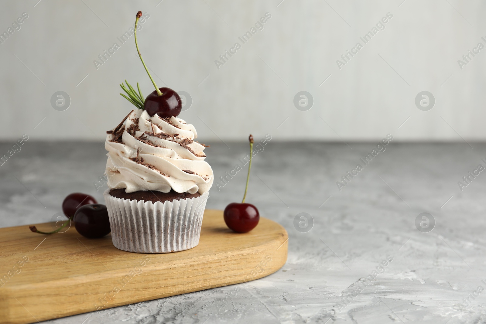 Photo of Delicious cupcake with cream and cherries on grey textured table. Space for text