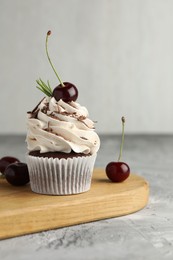 Photo of Delicious cupcake with cream and cherries on grey textured table