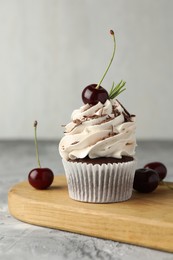 Photo of Delicious cupcake with cream and cherries on grey textured table