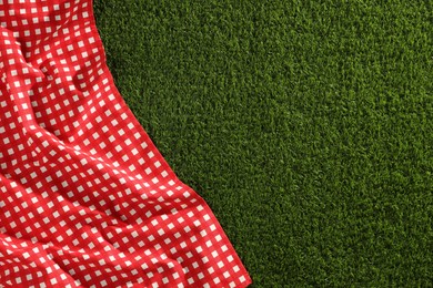 Photo of Checkered picnic tablecloth on green grass, top view. Space for text