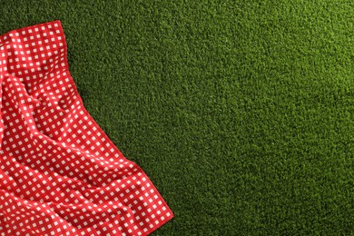 Photo of Checkered picnic tablecloth on green grass, top view. Space for text