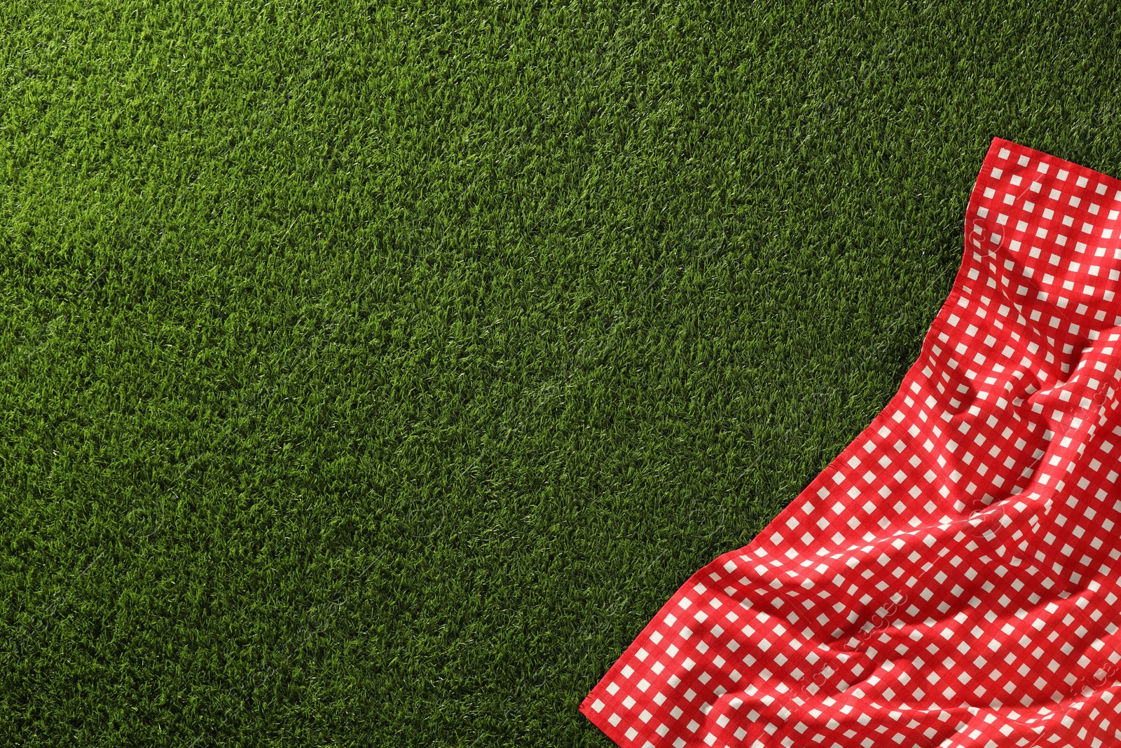 Photo of Checkered picnic tablecloth on green grass, top view. Space for text