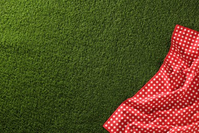 Photo of Checkered picnic tablecloth on green grass, top view. Space for text