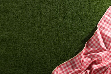 Photo of Checkered picnic tablecloth on green grass, top view. Space for text