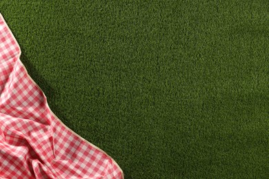 Photo of Checkered picnic tablecloth on green grass, top view. Space for text