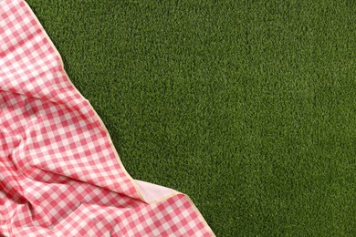 Photo of Checkered picnic tablecloth on green grass, top view. Space for text