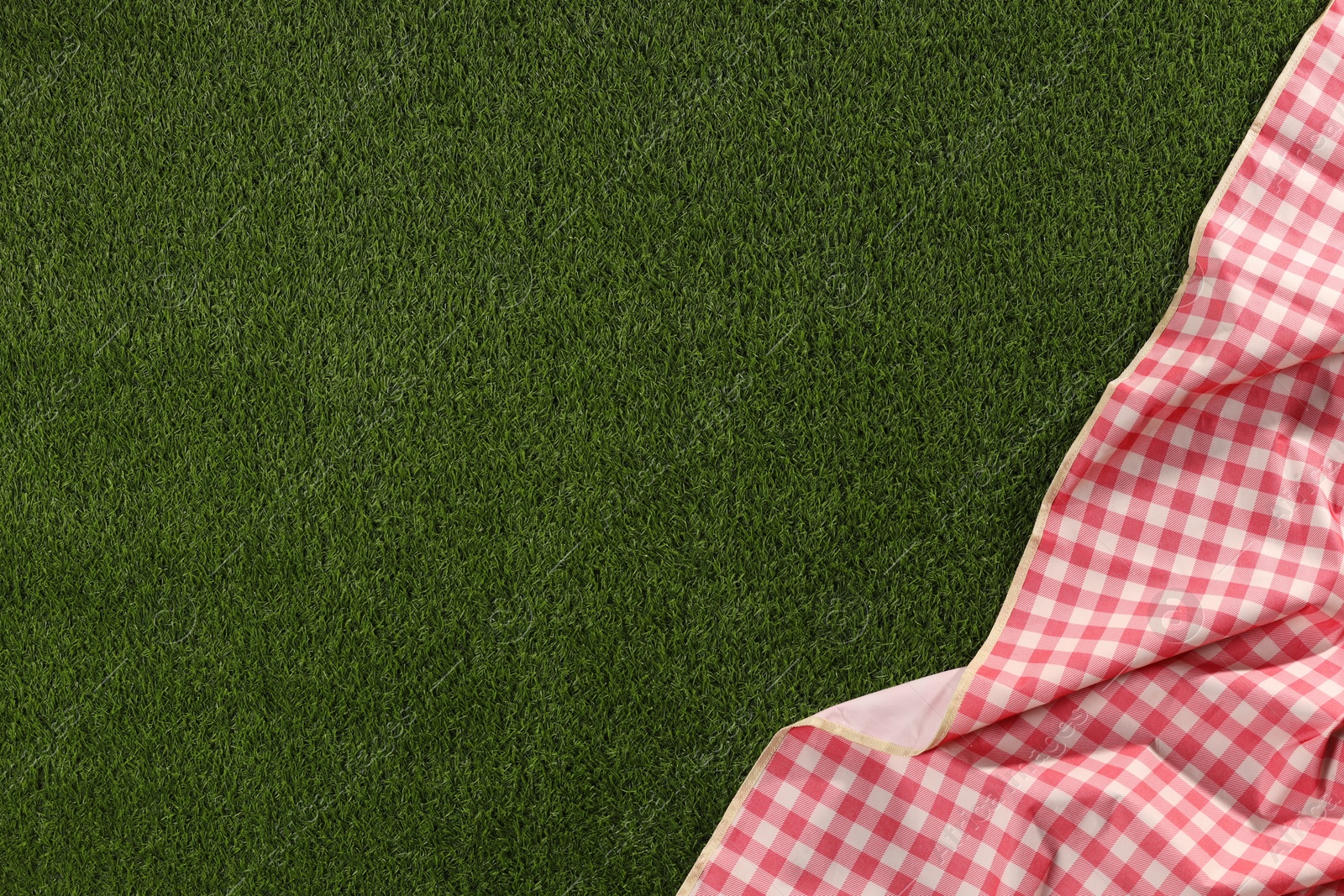 Photo of Checkered picnic tablecloth on green grass, top view. Space for text