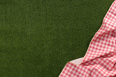 Photo of Checkered picnic tablecloth on green grass, top view. Space for text