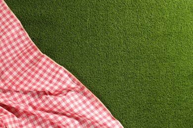 Photo of Checkered picnic tablecloth on green grass, top view. Space for text