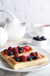 Tasty puff pastries with berries and tea on white marble table