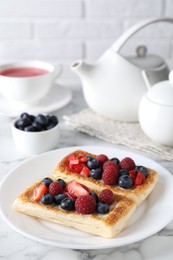 Photo of Tasty puff pastries with berries and tea on white marble table