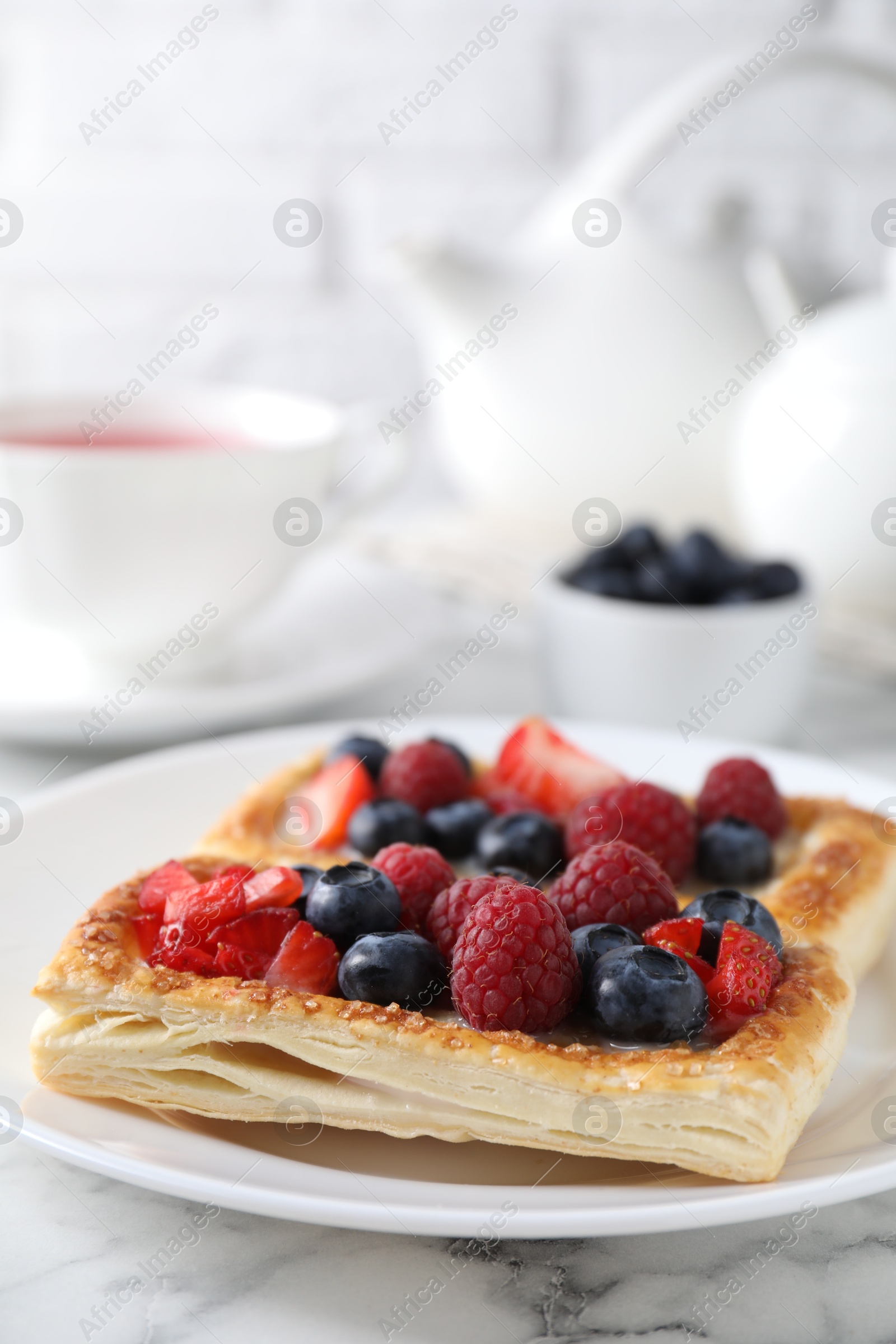 Photo of Tasty puff pastries with berries and tea on white marble table, closeup