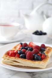 Photo of Tasty puff pastries with berries and tea on white marble table, closeup