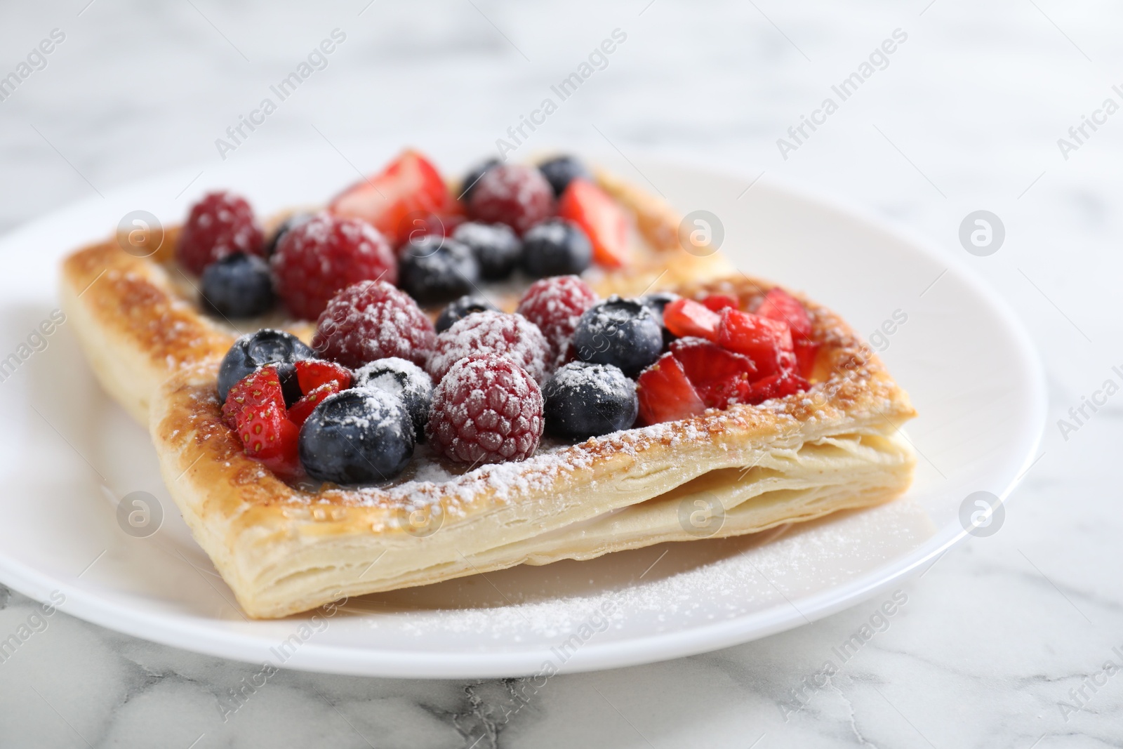 Photo of Tasty puff pastries with berries on white marble table, closeup