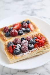 Tasty puff pastries with berries on white marble table, closeup