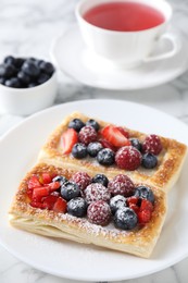 Photo of Tasty puff pastries with berries and tea on white marble table, closeup