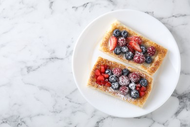 Tasty puff pastries with berries on white marble table, top view. Space for text