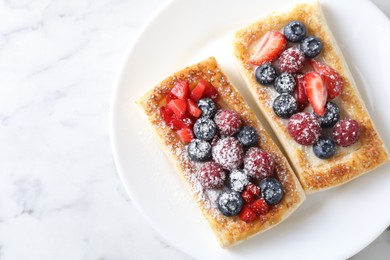 Tasty puff pastries with berries on white marble table, top view. Space for text