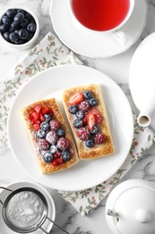 Photo of Tasty puff pastries with berries and tea on white marble table, flat lay