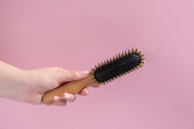 Woman holding brush with lost hair on pink background, closeup