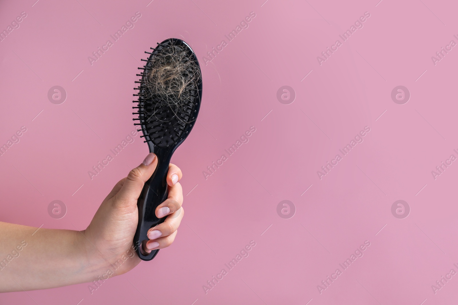 Photo of Woman holding brush with lost hair on pink background, closeup. Space for text