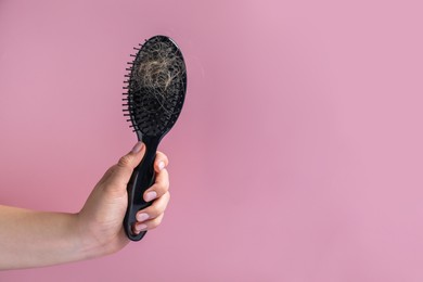 Woman holding brush with lost hair on pink background, closeup. Space for text