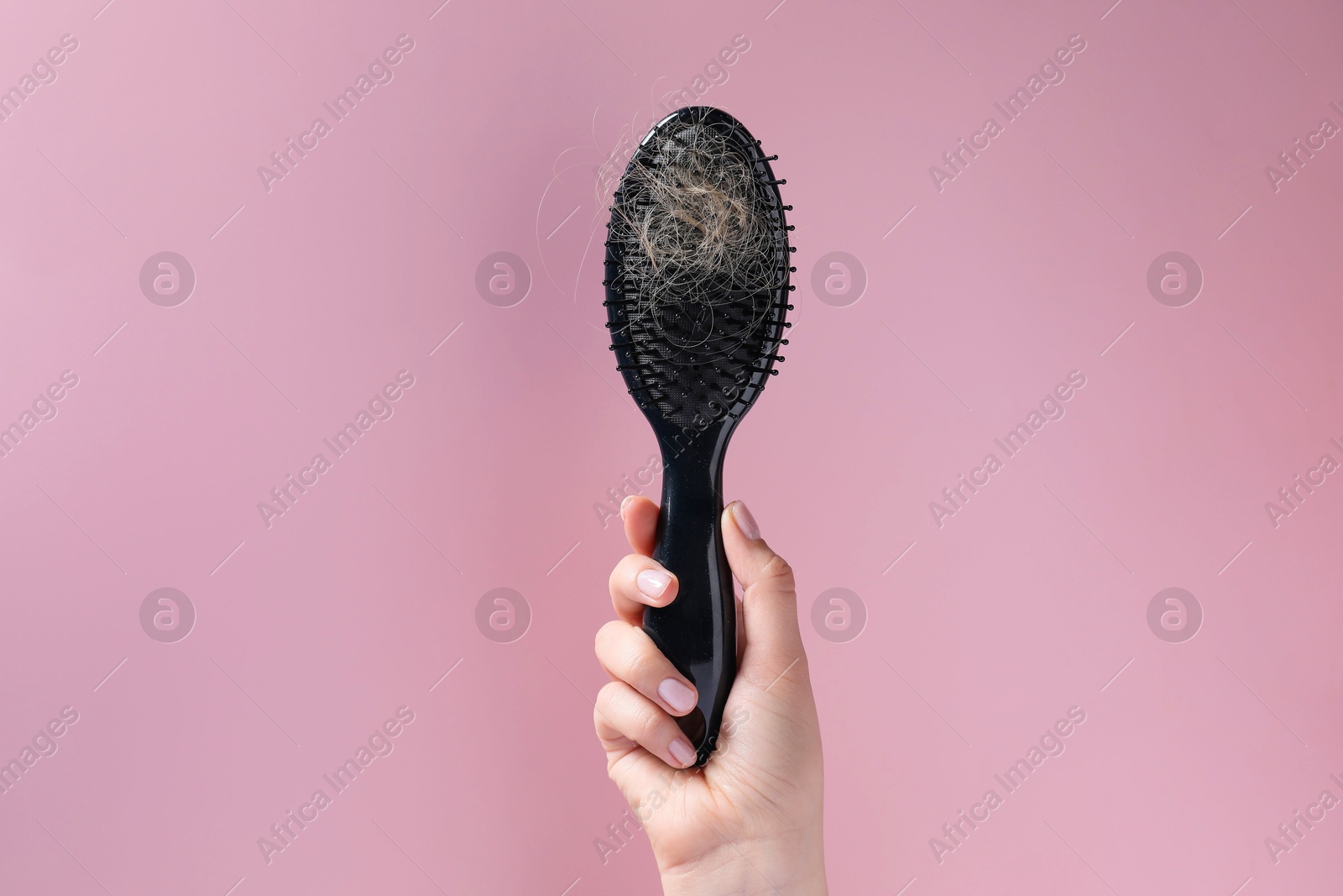 Photo of Woman holding brush with lost hair on pink background, closeup