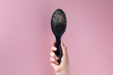 Photo of Woman holding brush with lost hair on pink background, closeup