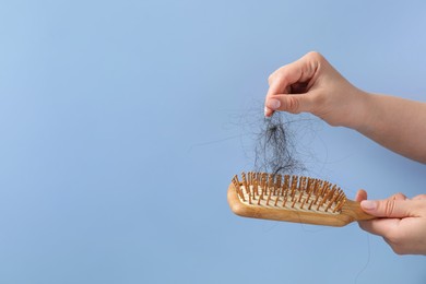 Photo of Woman taking her lost hair from brush on light blue background, closeup. Space for text