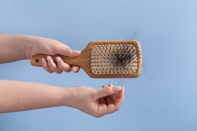 Photo of Woman taking her lost hair from brush on light blue background, closeup