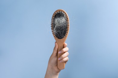 Woman holding brush with lost hair on light blue background, closeup