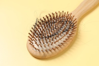 Photo of Wooden brush with lost hair on yellow background