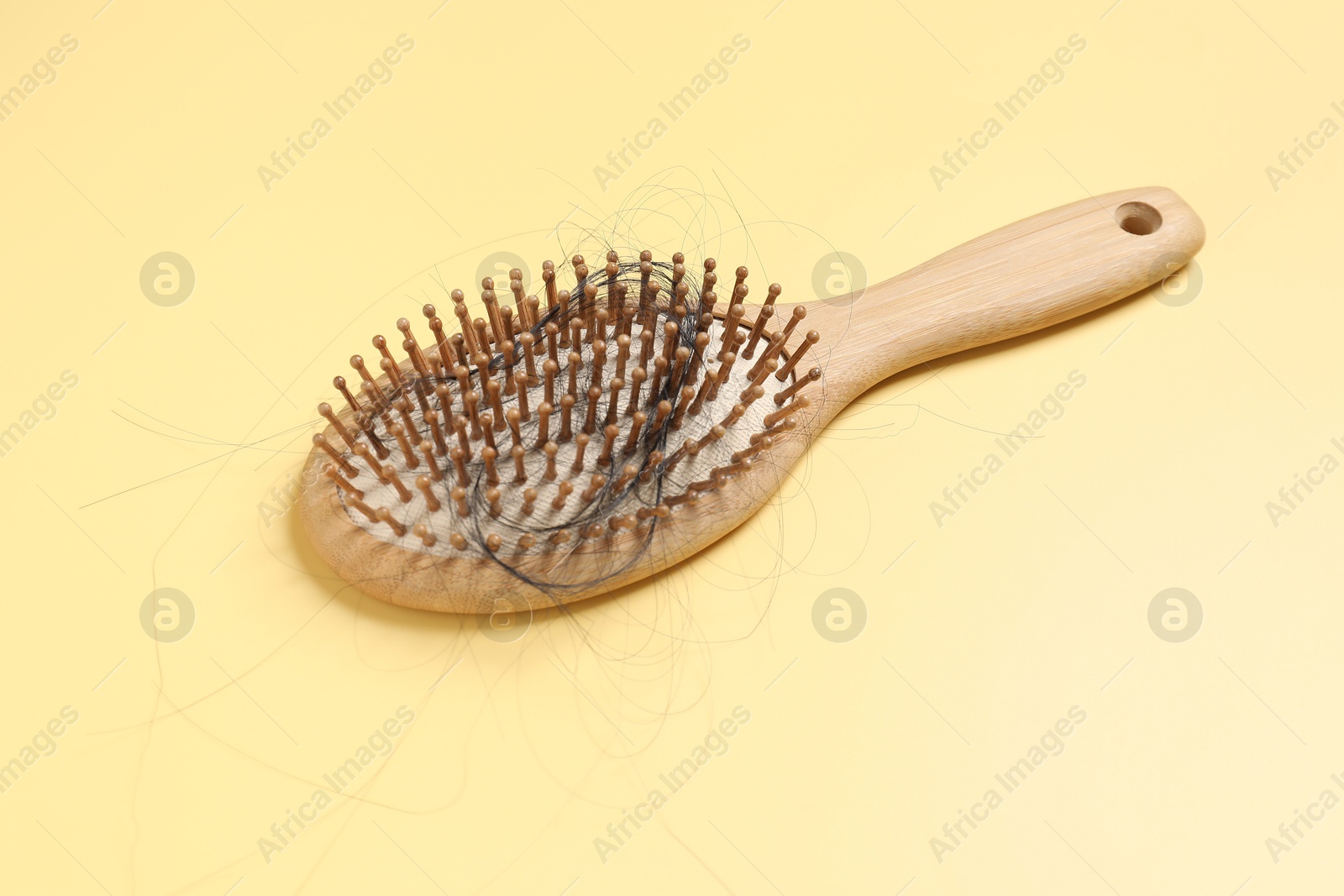 Photo of Wooden brush with lost hair on yellow background