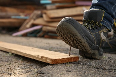 Photo of Careless worker stepping on nail in wooden plank outdoors, closeup