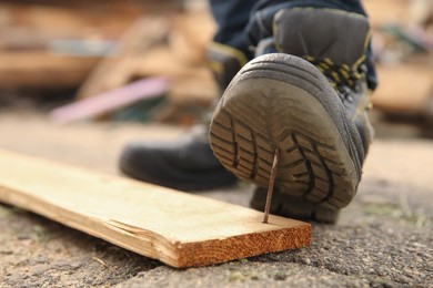 Photo of Careless worker stepping on nail in wooden plank outdoors, closeup