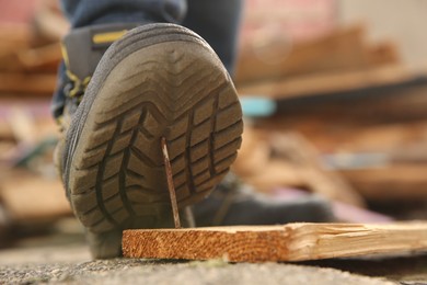 Careless worker stepping on nail in wooden plank outdoors, closeup