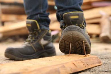 Careless worker stepping on nails in wooden plank outdoors, closeup