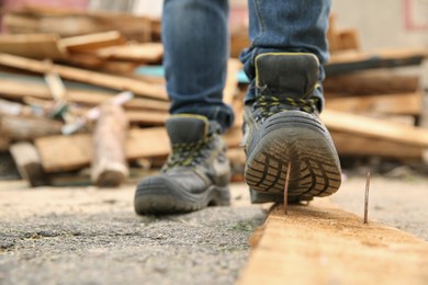 Careless worker stepping on nail in wooden plank outdoors, closeup