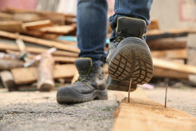 Photo of Careless worker stepping on nail in wooden plank outdoors, closeup