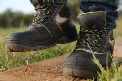 Careless worker stepping on nail in wooden plank outdoors, closeup