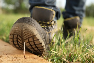 Photo of Careless worker stepping on nail in wooden plank outdoors, closeup