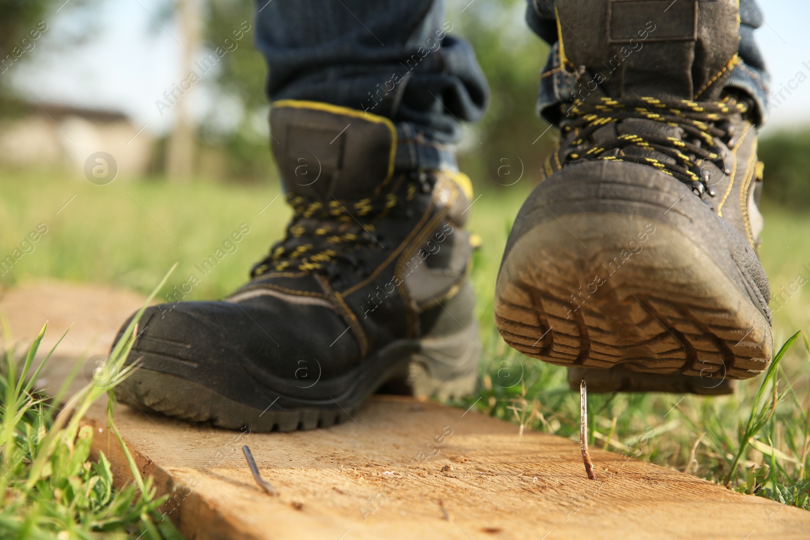 Photo of Careless worker stepping on nail in wooden plank outdoors, closeup